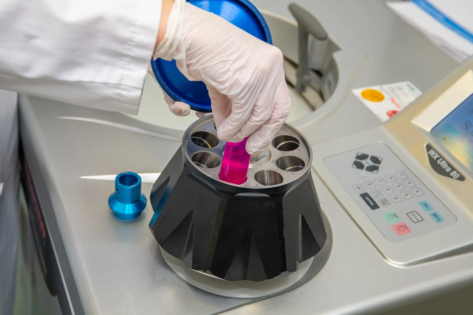 Eine Wissenschaftlerin und ein Wissenschaftler arbeiten hinter einer Glasfassade und mischen Chemikalien mit Großgeräten.